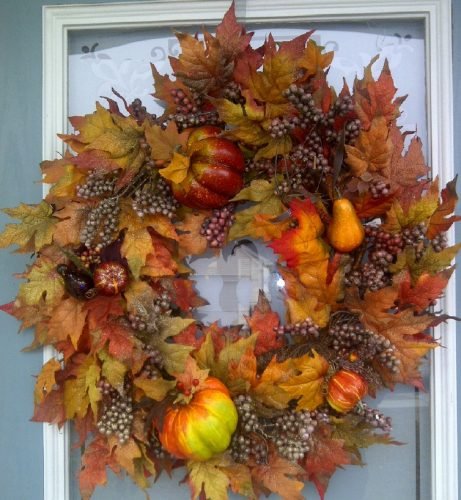 A charming front door in a Charleston home showcases a Thanksgiving wreath made of colorful leaves and pumpkins, welcoming the holiday spirit.