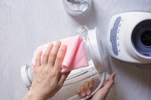 An individual cleaning a blender with a pink cloth in a Charleston home, showcasing effective blender cleaning tips.