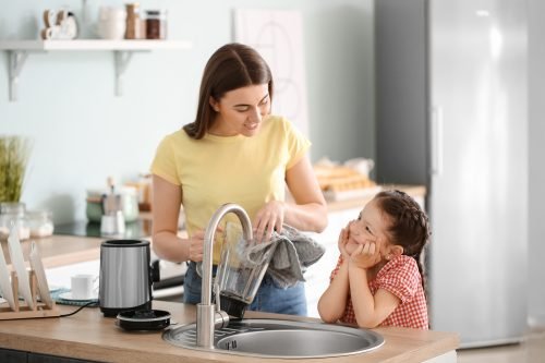 A woman and child collaborate to wash dishes in a sunny Charleston kitchen, embodying Blender Live Longer tips for a healthier lifestyle.