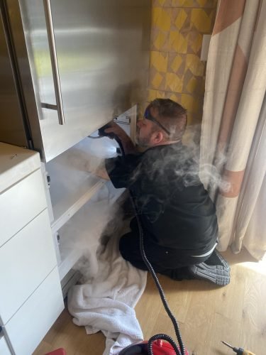 A man applies steam to clean the inside of a non functioning refrigerator in a Charleston home, preparing it for repair or disposal.