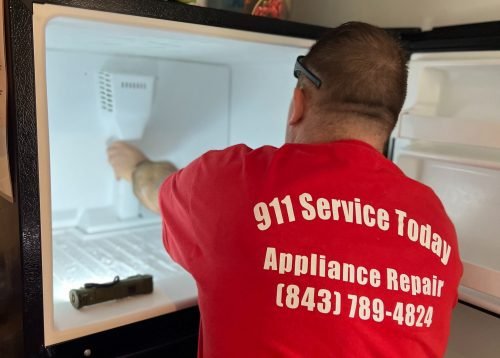 A man wearing a red shirt works on an ice maker in a Charleston home that is operating slowly, aiming to fix the appliance.