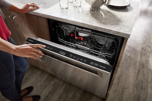A woman is seen opening the door of a KitchenAid dishwasher in a Charleston home, checking for any problems or maintenance needs.