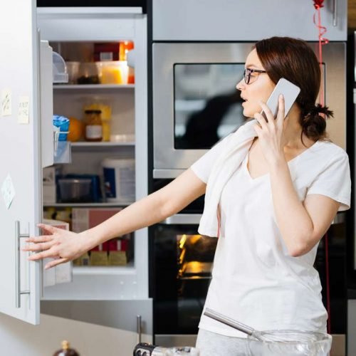 A woman converses on her cell phone while standing before an open refrigerator in a Charleston home, likely addressing Whirlpool appliance concerns.