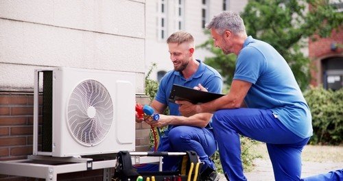 Two technicians in blue shirts performing maintenance on an air conditioning unit in a Charleston home, ensuring optimal HVAC system performance.