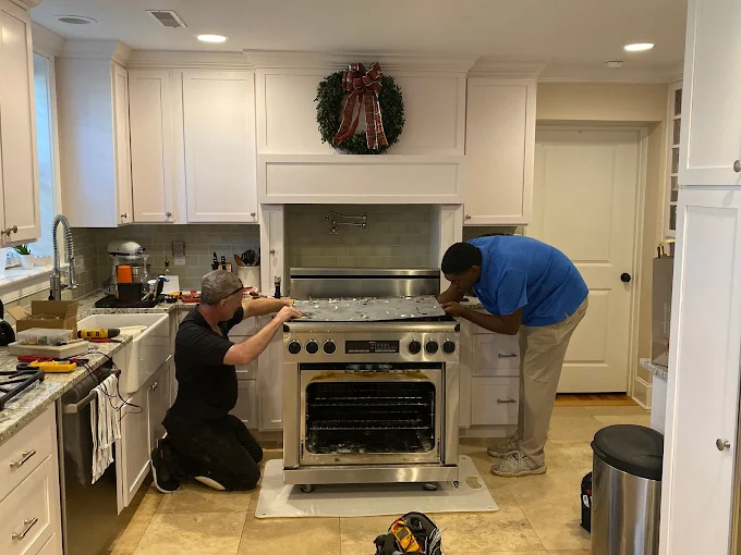 Two technicians repairing a kitchen oven, highlighting the appliance DIY danger of handling complex repairs without proper training.