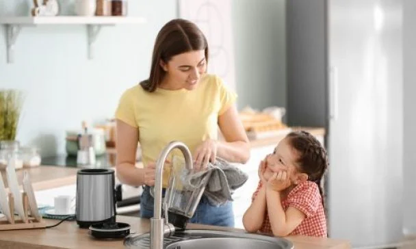 A woman and child collaborate to wash dishes in a sunny Charleston kitchen, embodying Blender Live Longer tips for a healthier lifestyle.