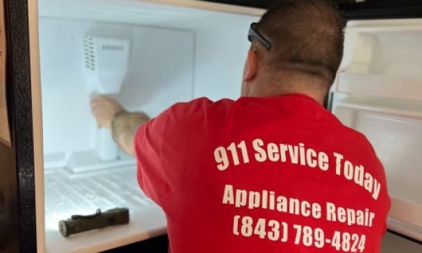 A man wearing a red shirt works on an ice maker in a Charleston home that is operating slowly, aiming to fix the appliance.