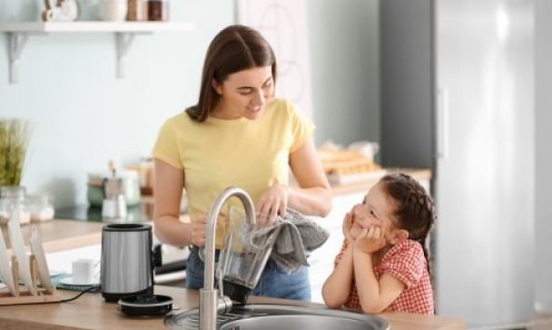 A woman and child collaborate to wash dishes in a sunny Charleston kitchen, embodying Blender Live Longer tips for a healthier lifestyle.