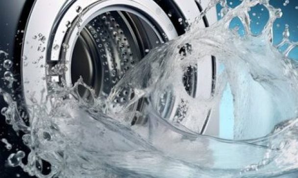 Water splashes from a washing machine in a Charleston home, highlighting a problem with drainage that requires fixing.