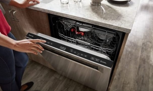 A woman is seen opening the door of a KitchenAid dishwasher in a Charleston home, checking for any problems or maintenance needs.