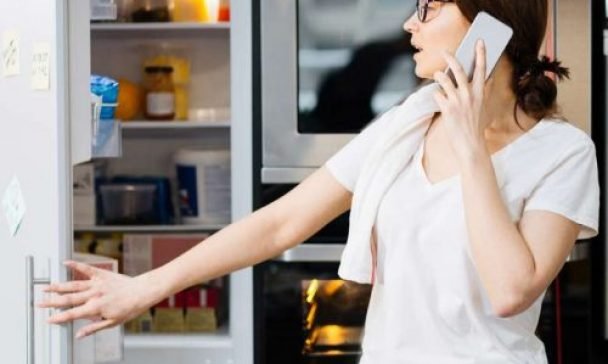 A woman converses on her cell phone while standing before an open refrigerator in a Charleston home, likely addressing Whirlpool appliance concerns.